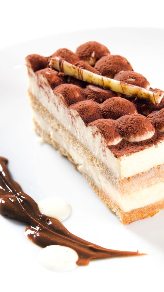 A classic tiramisu dessert with layers of coffee-soaked ladyfingers and mascarpone cream, garnished with cocoa powder and chocolate shavings.